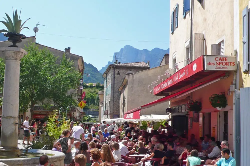 Photographie d'une fontaine en pierre et d'un bar typique du sud de la France